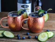 two copper mugs filled with blueberries and cucumbers