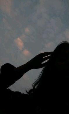 the silhouette of a woman holding her hair in front of a blue sky with clouds