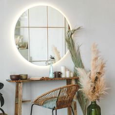 a round mirror sitting on top of a wooden table next to a chair and vase