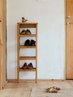 a wooden shelf with shoes on it next to a door and rug in front of it