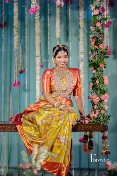 a woman sitting on top of a wooden bench in front of flowers and garlands