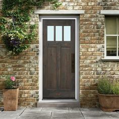 a wooden door sitting next to two potted plants on the side of a brick building