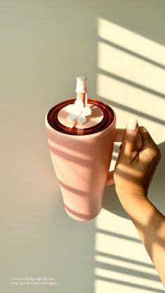 a hand holding a pink cup with two white cups on it and the top half is being held up