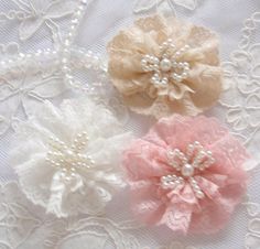 three different colored flowers on a white lace table cloth with pearls and beads in the center