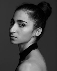 a black and white photo of a woman with her hair in a high bun, looking at the camera