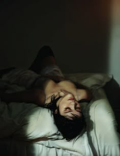 a man laying on top of a bed in the dark with his head down and eyes closed