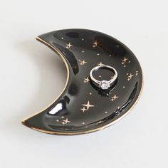 a black and gold plate with a ring on top of the moon shaped dish that has stars all over it