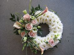 a white wreath with pink roses and green leaves on the top is laying on the ground