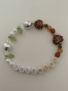 a beaded bracelet with beads and leaves is shown on a white surface, the words mom spelled out in gold letters