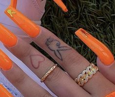 two women's hands with orange nail polishes on their fingers and one has an arrow tattoo