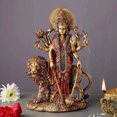 a statue of the hindu god sitting on a table with flowers and candles in front of it