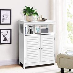 a small white cabinet in a living room with pictures on the wall and a potted plant