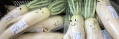 several vegetables with faces drawn on them in plastic bags at a market stall, including asparagus and cucumbers