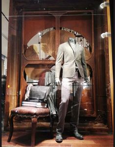 a mannequin dressed in a suit and tie standing next to a wooden chair