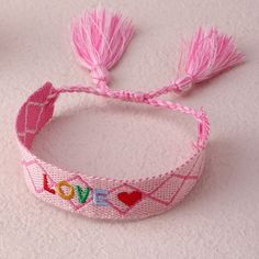 a pink bracelet with the word love written on it and two tassels attached