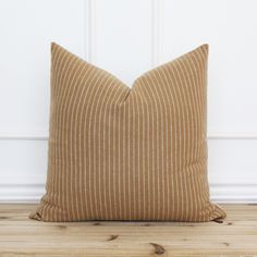 a brown and white striped pillow sitting on top of a wooden floor next to a wall