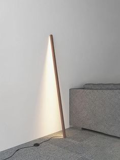 a floor lamp sitting on top of a gray couch next to a white wall with a wooden pole