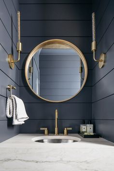 a bathroom sink under a round mirror with gold faucets on the wall next to it