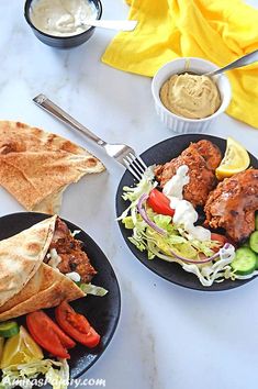 two black plates filled with different types of food on a white tablecloth and yellow napkins