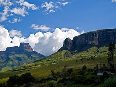 the mountains are covered with green grass and clouds in the distance, as seen from below