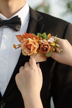 a man in a tuxedo adjusts his boutonniere with flowers