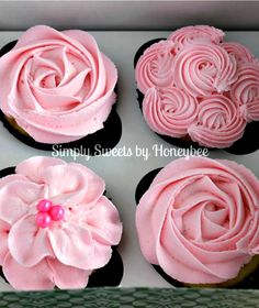 four cupcakes with pink frosting and flowers on top are in a box