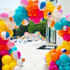 an archway decorated with balloons and streamers in front of a welcome to summer sign