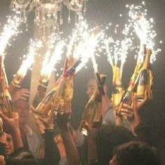 a group of people holding up champagne bottles with sparklers in the air at night