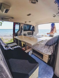 a woman sitting in the back of an rv looking out at the ocean from inside