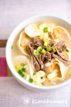 a white bowl filled with soup and meat on top of a wooden table next to chopsticks