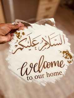 a person holding up a sign that says welcome to our home in arabic and english