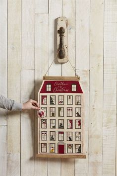 a person is holding up a wooden calendar with pictures on it and a bottle opener hanging from the wall