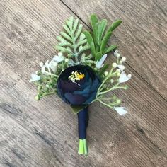 a blue boutonniere with white flowers and green leaves on a wooden surface