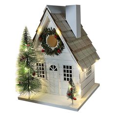 a small white house with christmas decorations on the roof and trees in front of it