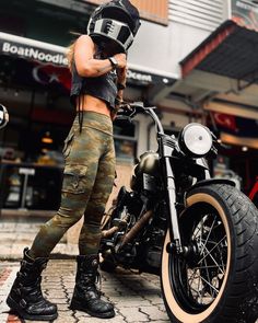 a man in camo pants standing next to a black and gold motorcycle on the street