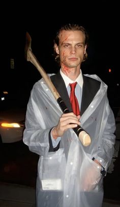 a man dressed up as a zombie holding a large hammer and wearing a plastic coat