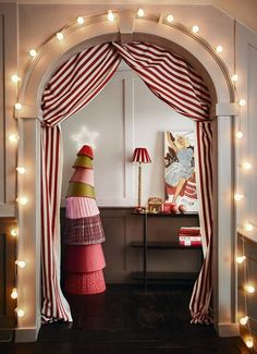 a christmas tree in the corner of a room with lights around it and a red and white striped curtain