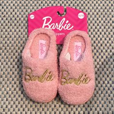 a pair of pink slippers with gold lettering on the front and bottom, sitting on a carpet