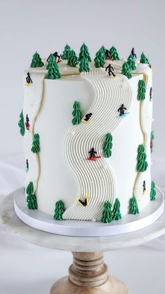 a white cake with green trees and skiers on it