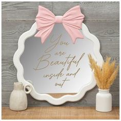 a mirror with a pink bow on it sitting next to a vase and some flowers