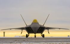 a fighter jet sitting on top of an airport tarmac at sunset with the sky in the background