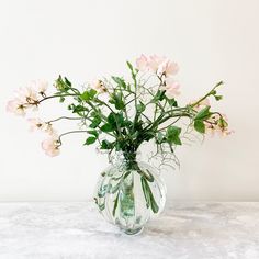 a glass vase filled with pink flowers on top of a white countertop next to a wall