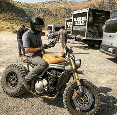 a man riding on the back of a motorcycle next to other vehicles and people standing around