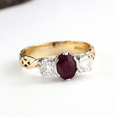 a three stone ring with an oval shaped ruby and two smaller round diamonds on the side