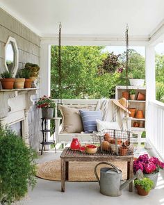 an outdoor porch with potted plants and hanging baskets on the porch swing, surrounded by greenery