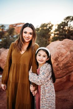 mother and daughter standing in front of red rocks at sunset with their arms around each other