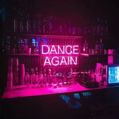 a neon sign that says dance again in front of bottles and glasses on a shelf