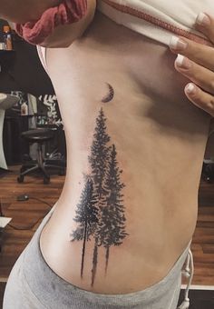 a woman with a pine tree tattoo on her stomach and the moon in the background