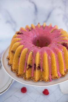 a bundt cake with raspberry icing on a white plate next to plates