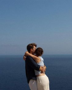 a man and woman embracing each other in front of the ocean